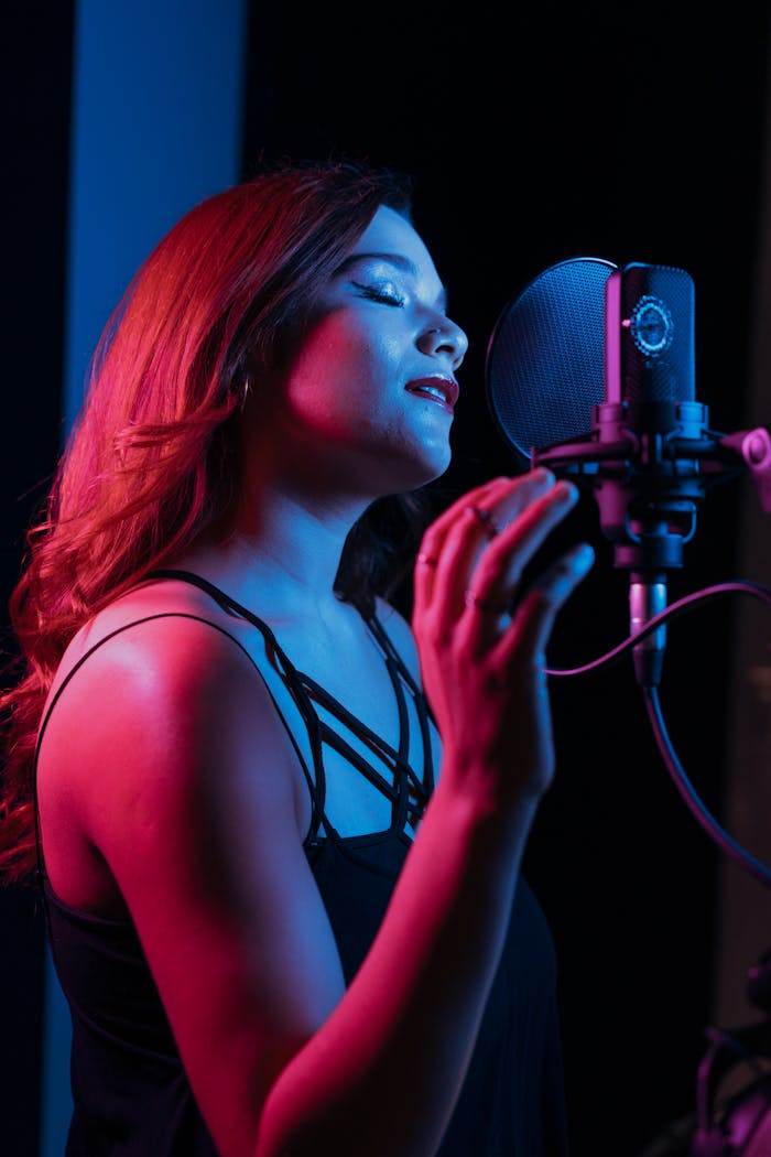 Young female singer in a recording studio, passionately singing into a microphone with closed eyes.